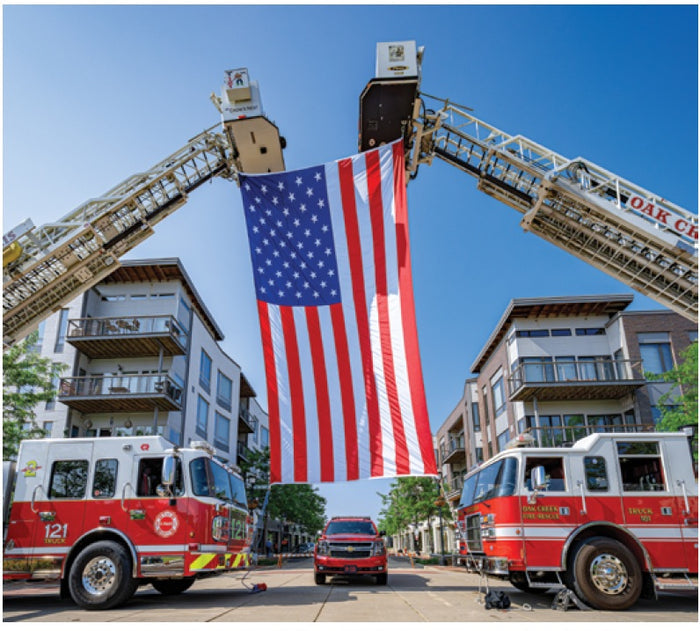 Two fire trucks with an American flag between them against a blue sky.