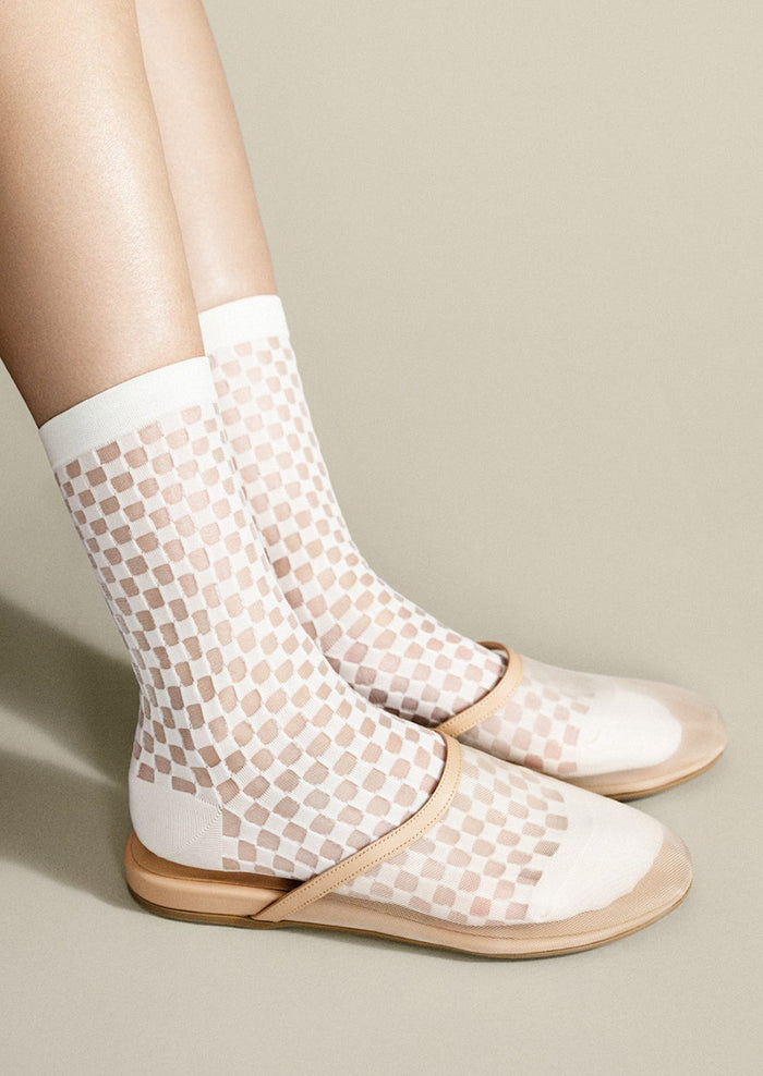 White fishnet socks with beige pattern worn with flat sandals on a neutral background