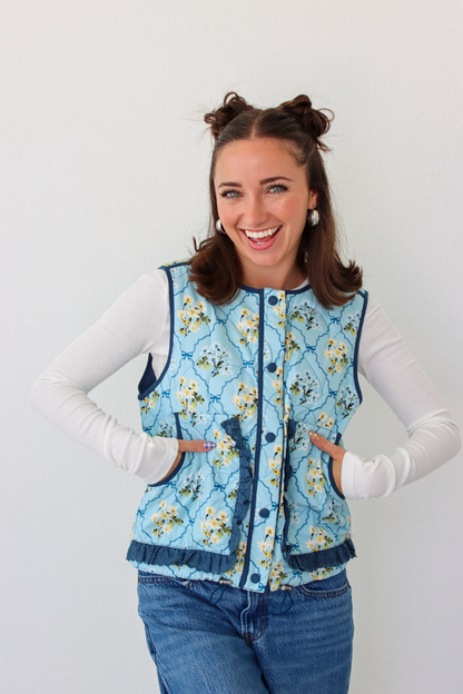 Woman wearing a blue floral puffer vest with a white long sleeve shirt and blue denim jeans