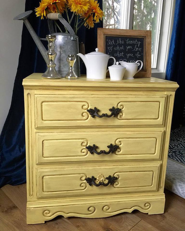 Quart container of Retique It Naples Yellow furniture and cabinet paint with brush strokes on a painted wooden surface.