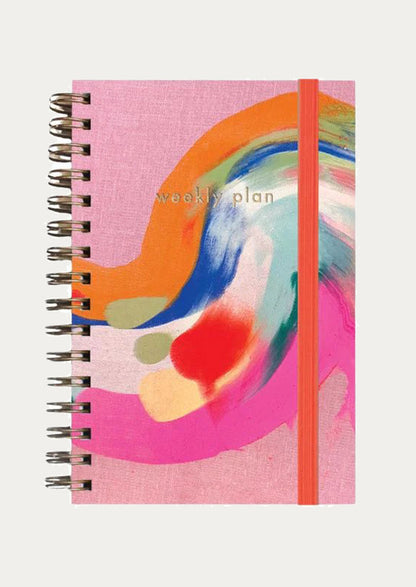Notebook with abstract design and 'weekly plan' text on a pink background