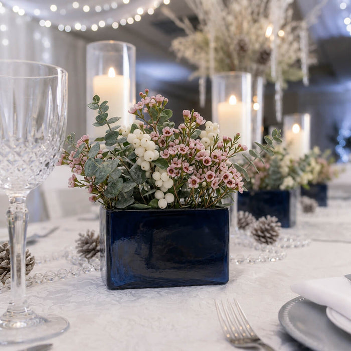 Navy blue square vase holding pink waxflowers and white berries as a winter centerpiece