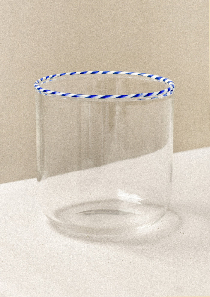 A clear drinking glass with a blue striped rim