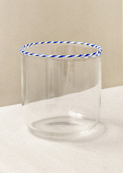 A clear drinking glass with a blue striped rim