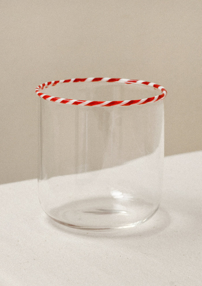 A clear drinking glass with a red striped rim