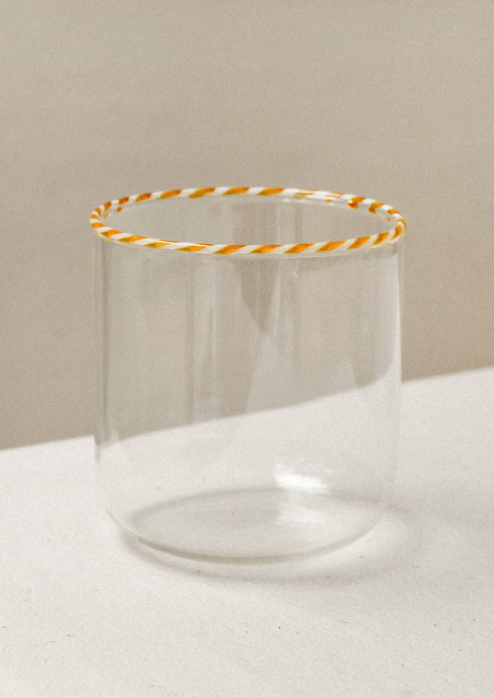 A clear drinking glass with an orange striped rim