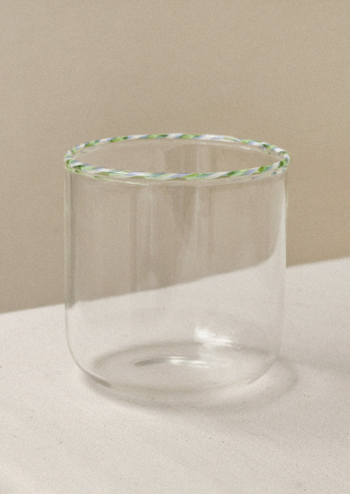A clear drinking glass with a green striped rim