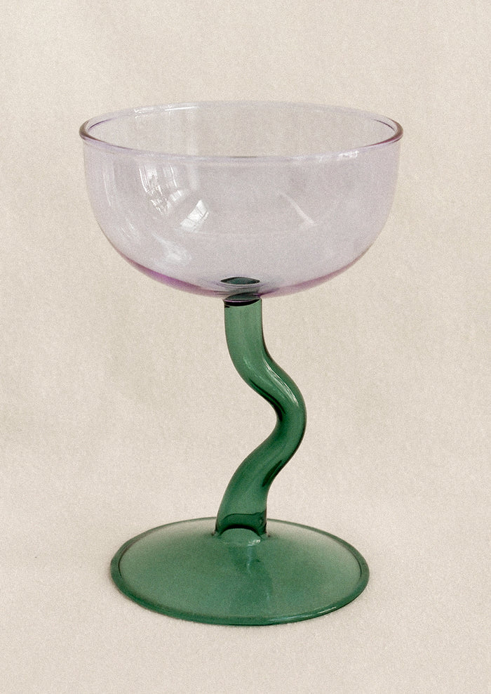 Glass with purple bowl and green stem on a beige background
