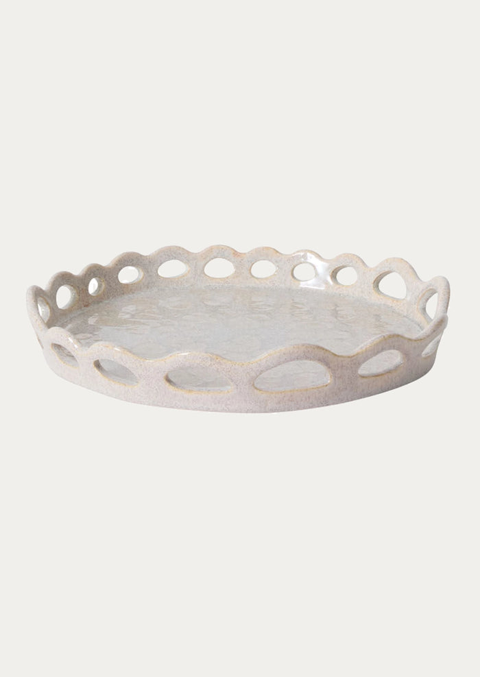 A round ceramic tray with a scalloped edge and cutout details, shown on a plain light gray background.
